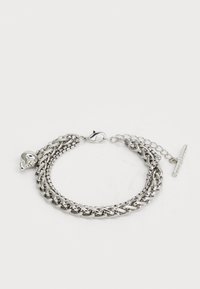 Bracelet en chaîne en métal argenté avec un design superposé. Présente un charmant crâne et un fermoir à bascule. Texture lisse et finition polie.