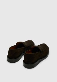 Chaussures en daim marron à enfiler avec un bout rond, des coutures apparentes et une semelle en caoutchouc noire lisse. Intérieur doté d'une doublure douce de couleur fauve.