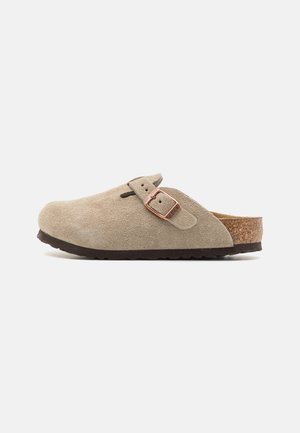 Beige Wildleder-Birkenstock mit runder Zehenpartie, seitlichem Schnallendetail und Korkfußbett. Ausgestattet mit einer strukturierten braunen Gummisohle.