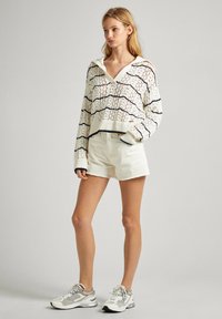 Sudadera con capucha de punto en color crema con rayas marinas, combinada con pantalones cortos beige y zapatillas grises. La sudadera tiene un corte relajado y puños acanalados.