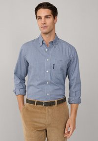 Camisa de cuadros azul y blanca de manga larga con cuello abotonado, bolsillo frontal y puños enrollados, combinada con pantalones de corduroy marrón claro y un cinturón.