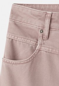 I jeans in denim rosa pallido presentano una tasca frontale, passanti per cintura e una chiusura con bottone metallico. Il tessuto ha un aspetto testurizzato e rigato.