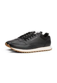 Sneaker nere in pelle con finitura testurizzata, dotate di una intersuola bianca e suola esterna in gomma marrone; includono lacci neri e dettagli di branding.
