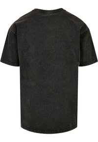 T-shirt en coton noir avec un col rond, des manches courtes et une texture légèrement délavée. Présente des coutures visibles le long du col et des manches.