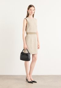 Beige tweed-mekko, jossa on istuva vyötärö, musta kudottu käsilaukku ja mustat kärkitossut. Sujuva pinta, yksinkertainen muotoilu, minimaliset korostukset.
