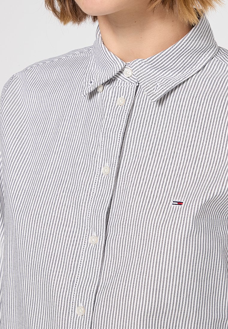 Camicia a righe con motivo bianco e blu navy, materiale in cotone morbido, colletto a punta e piccolo logo sul petto.