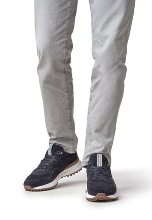 Baskets en daim bleu marine avec semelles blanches, présentant un design texturé, des lacets et un accent rayé noir et blanc sur la languette.