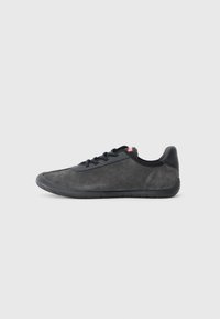 Baskets en suède noir avec une tige texturée, semelle en caoutchouc et bout rond. Présente des lacets noirs et une subtile accent rouge près du talon.