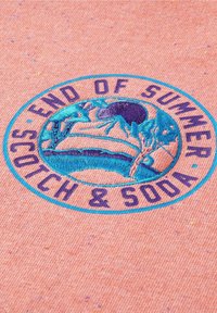 Rund broderad patch på persikofärgad tyg med turkos och lila design av träd vid vatten och texten "SISTA DAGARNA AV SOMMAREN SCOTCH & SODA."