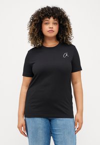 Μαύρο βαμβακερό μπλουζάκι με κοντό μανίκι, στρογγυλή λαιμόκοψη και μικρό λευκό λογότυπο 'ck' στην αριστερή πλευρά του στήθους. Φοριέται με ανοιχτό μπλε τζιν.