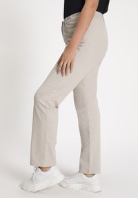 Pantaloni beige a gamba dritta realizzati in tessuto morbido, dotati di tasche frontali e chiusura con zip, abbinati a sneaker bianche.