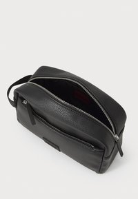 Black leather toiletry bag with a textured surface, double zip closure, and a front pocket. Open, revealing a red interior lining.