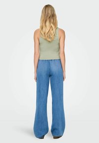 Débardeur ribbed vert clair associé à un jean large bleu clair. Le haut présente une coupe ajustée, tandis que le jean a une coupe décontractée.