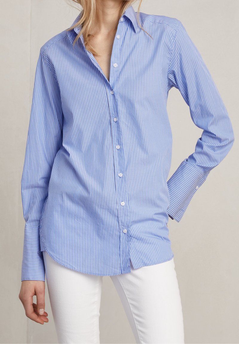 Světle modrá košile na knoflíky s bílými svislými pruhy. Obsahuje špičatý límec, dlouhé rukávy a zaoblený lem s uvolněným střihem.
