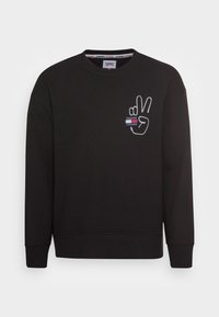 Felpa nera con collo a girocarsico, dotata di simbolo della pace ricamato in bianco e logo Tommy Jeans sul lato sinistro del petto. Polsini e orlo a coste.