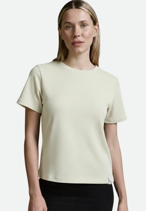 Kurzärmliges, cremefarbenes T-Shirt aus strukturiertem Material, mit rundem Halsausschnitt und einem kleinen Etikett in der unteren linken Ecke.