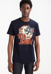 T-shirt in cotone blu navy con grafica vintage di "Tom and Jerry" che presenta personaggi dei cartoni animati e testo in rilievo con accenti rossi e gialli.