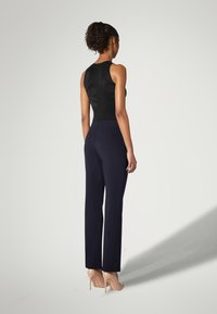 Sort ærmeløs top med udskæringsdesign, kombineret med højtaljede marineblå bukser og nøgenfarvede højhælede sko. Glatte teksturer hele vejen igennem.