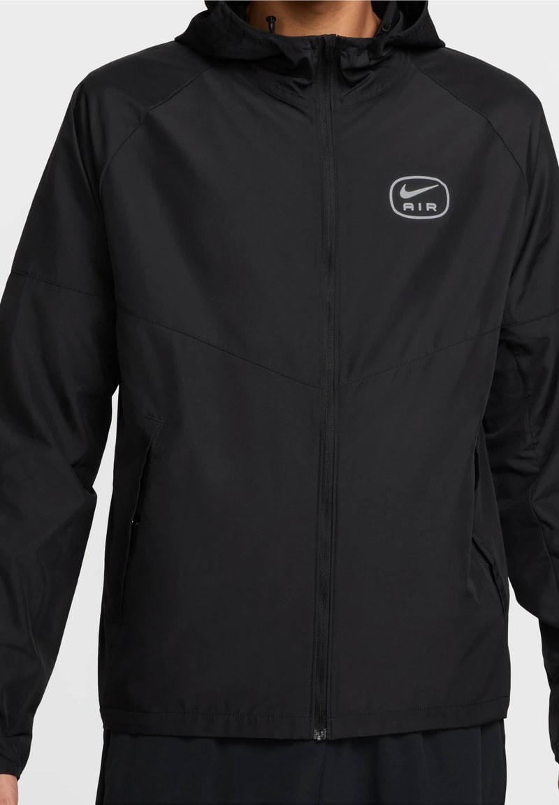 Veste légère noire à capuche avec fermeture éclair frontale intégrale, poches latérales et logo blanc Nike Air sur la poitrine gauche.