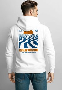 White hoodie featuring a graphic on the back with wavy blue lines, an orange sun, and the text "CALIFORNIA slow days at the beach."