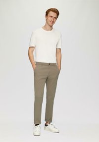 T-shirt blanc à manches courtes, pantalon slim gris clair, et sneakers blanches avec des accents bleu marine. La tenue présente un design moderne et décontracté.