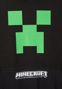 Sweatshirt nero con un grande design della faccia di Creeper verde. Include un tessuto testurizzato e un logo "Minecraft" bianco nella zona taschino.