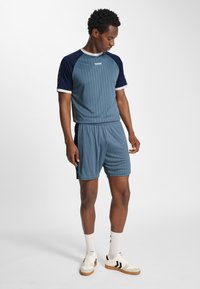 Blå och marinblå sportoutfit med horisontella ränder, korta ärmar och resår i midjan. Inkluderar vita detaljer och sportiga skor.