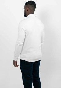 Witte poloshirt met lange mouwen en een zijsplitrand, gecombineerd met marineblauwe broek, gezien van achteren. Gladde stof en een smal ontwerp.
