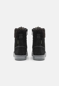 Botas de ante negro con un collar texturizado y esponjoso, que cuentan con un diseño impermeable y una suela moteada. Detalle de cremallera en la parte trasera.