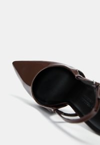 Brun lackläder pumps med spetsig tå och en smidig design, med svart inredning och en smal ankelrem för en säker passform.