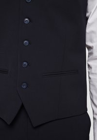Marines waistcoat gemaakt van gladde stof, met zes knopen, twee smalle zijzakken en een scherpe V-halslijn met subtiele stikdetails.