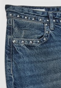 Džínová sukňa s tmavomodrou farbou, ozdobená striebornými cvočkami na páse a prednom vrecku, s klasickým dizajnom s piatimi vreckami.