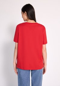 Camiseta corta roja de manga corta con escote redondo, corte relajado y textura suave. Combinada con jeans de mezclilla azul claro.