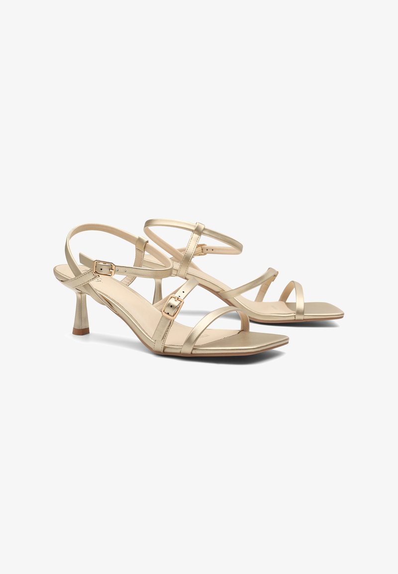 Zlaté metalické vysoké sandále na podpätku s viacerými nastaviteľnými popruhmi, štvorcovou špičkou a štíhlym podpätkom. Hladký povrch s minimálnymi akcentmi.