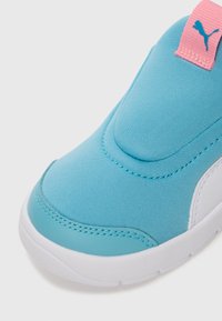 Gros plan sur l'orteil d'une sneaker bleue et blanche avec un logo Puma rose sur l'onglet de traction et une semelle en caoutchouc blanche.