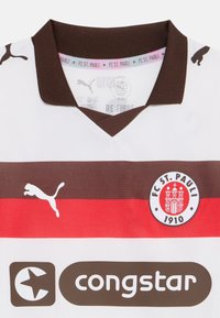 FC St. Pauli focimeze, fehér alapon barna és piros csíkokkal, v-nyakkivágással, Puma logóval, klub címkéjével és "congstar" logóval sötétbarnában.