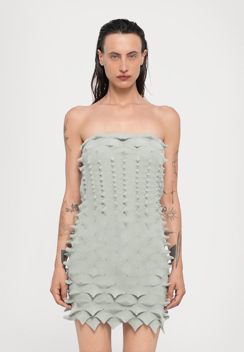 Vestido sin tirantes, ajustado, en tejido color verde claro, con una superficie texturizada que presenta patrones ondulados en capas y pequeños acentos reflectantes.