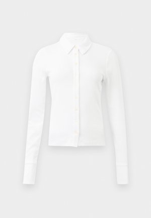 White long-sleeve shirt with a button-up front, featuring a collar, soft ribbed texture, and light yellow buttons.