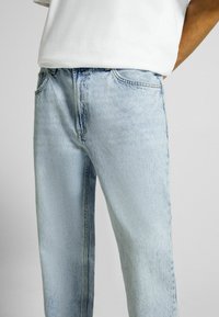 Jeans de mezclilla azul claro con un corte relajado, que presentan un lavado ligeramente desgastado, diseño de cinco bolsillos y costuras visibles.