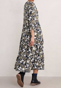 Sukienka maxi w oliwkowym kolorze w kwiaty, z rękawami o długości trzech kwart, warstwowy design, wzory białych i granatowych kwiatów, zestawiona z czarnymi botkami za kostkę.