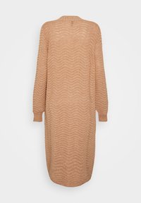Beige stickad klänning med ett texturerat vågmönster, lös passform, långa ärmar och rundad halsringning. Bakom har den en design som når till mitten av vaden.