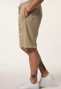 Beige cotton shorts with elastic waistband, side pockets, and an embroidered logo. Pairing with white sneakers.