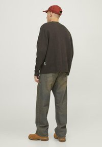 Maglione lavorato a maglia marrone scuro con orlo e polsini a coste, abbinato a jeans grigi larghi e stivali marroni. Presenta un berretto rosso.