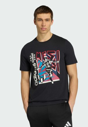 Nuori mies, joka pukeutunut mustaan Adidas-jalkapallopaitaan, jossa on värikäs grafiikka jalkapalloilijasta ja "MESSI"-teksti.