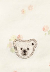 Visage d'ours blanc brodé avec contour gris sur un tissu décoré de petits motifs floraux pastel roses et verts.