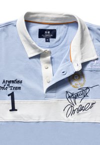 Light blue polo shirt with a white collar, featuring embroidered text "Argentina Polo Team" and number "1," adorned with signatures and logo detail.