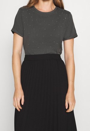 Szara koszulka z krótkim rękawem i okrągłym dekoltem, ozdobiona rozsianymi kryształkami na piersi, noszona z czarną plisowaną spódnicą.