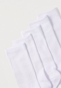 Fehér pamut zokni bordás szegélyekkel, sima textúrával és testhezálló kialakítással. Öt pár egymásra helyezve világos háttéren.
