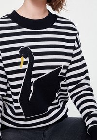 Czarny i biały sweter w paski z dużym czarnym łabędziem z żółtym dziobem. Prążkowany okrągły dekolt i luźny krój.