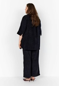 Top in velluto a coste nero con maniche corte, abbinato a pantaloni a gamba larga coordinati. Il tessuto presenta un motivo a coste testurizzato e una leggera lucentezza.